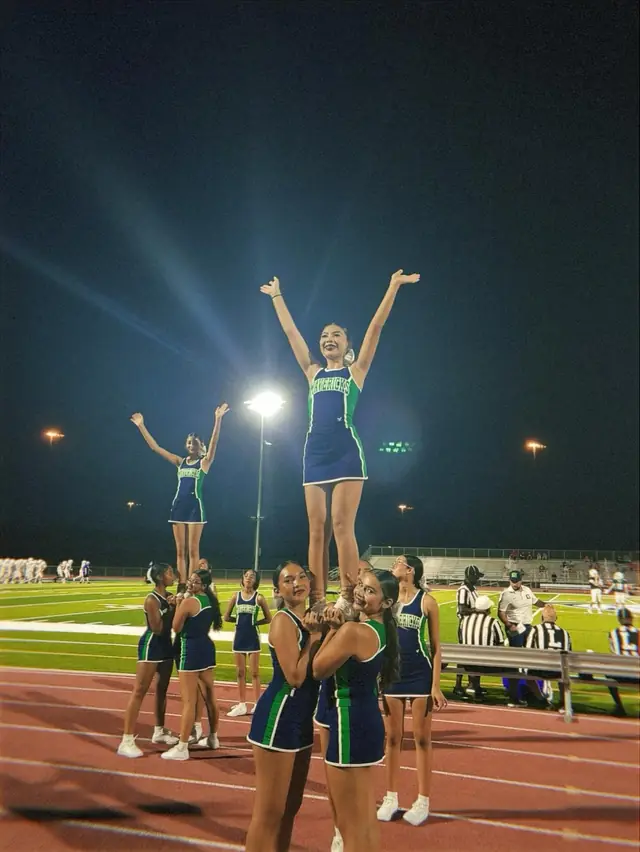 Two stunt groups hold their flyers up under the stadium lights at a night game